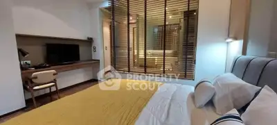 Modern bedroom with stylish decor and open view to bathroom, featuring a cozy bed and workspace.