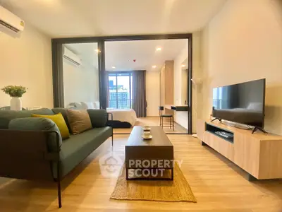 Modern living room with stylish decor and open view to bedroom, featuring sleek furniture and natural light.