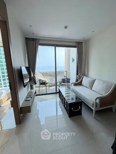 Modern living room with ocean view, sleek furniture, and large glass doors opening to a balcony.