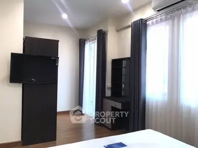 Modern bedroom with sleek furniture and natural light, featuring a wall-mounted TV and stylish curtains.