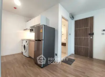 Modern apartment kitchen with fridge, washing machine, and wooden flooring