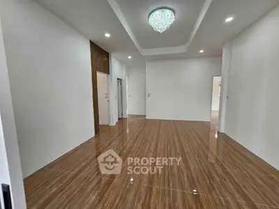 Spacious modern living room with elegant chandelier and polished wooden flooring.