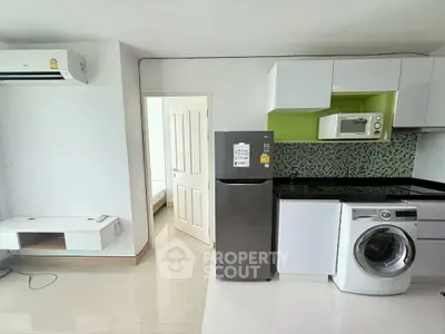 Modern apartment kitchen with sleek appliances and open layout, featuring washing machine and fridge.