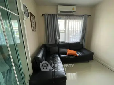 Cozy living room with black leather sofa and air conditioning, perfect for relaxation.