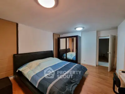 Spacious bedroom with modern furnishings and wooden flooring, featuring a large bed and mirrored wardrobe.