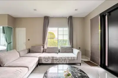 Spacious modern living room with elegant gray sofa and marble coffee table, featuring large window with garden view.