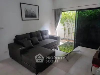 Modern living room with sleek black sofa and glass coffee table, opening to a lush garden view.