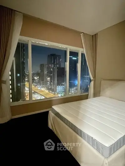 Luxurious bedroom with stunning city view from large window, perfect for urban living.