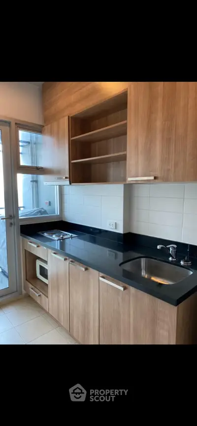 Modern kitchen with sleek wooden cabinets and black countertops, featuring a built-in microwave and ample storage space.
