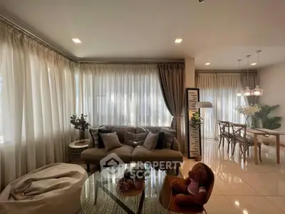 Elegant living room with plush sofa and dining area, featuring soft lighting and modern decor.