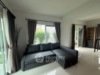 Spacious living room with modern sofa and large windows offering garden views.