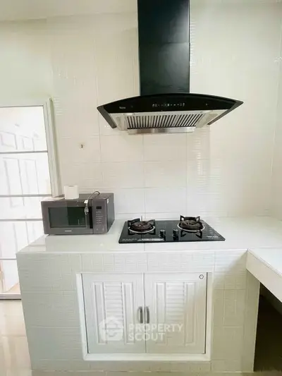 Modern kitchen with sleek gas stove and microwave, featuring a stylish range hood and white cabinetry.