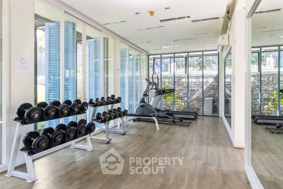Spacious gym with modern equipment and large windows in luxury residential building.