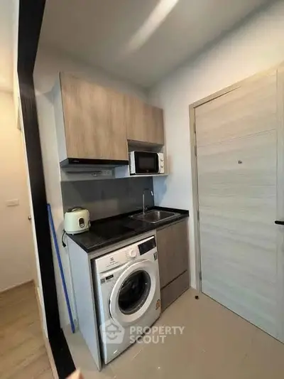 Compact modern kitchen with washing machine and microwave in sleek apartment.