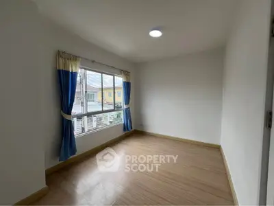 Bright empty room with large window and wooden flooring, ideal for customization.