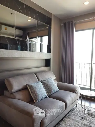 Modern living room with plush gray sofa and stylish decor, featuring large windows and elegant curtains.