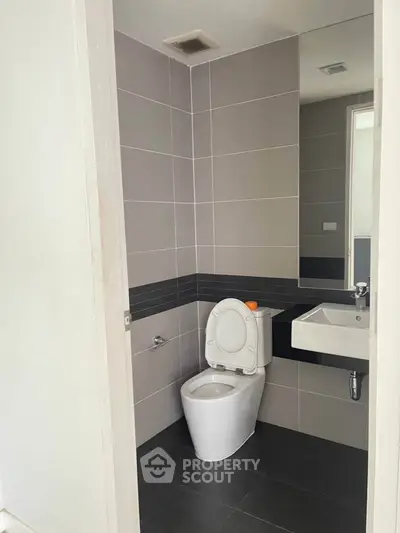 Modern bathroom with sleek design and neutral tiles, featuring a toilet and sink.