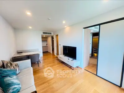 Modern living room with wooden flooring, stylish furniture, and sliding door to kitchen.