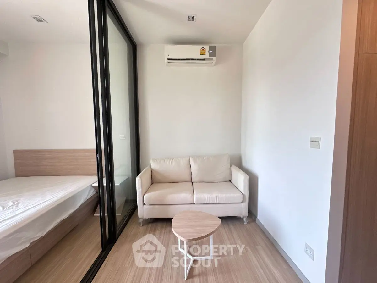Modern compact living room with cozy sofa and glass partition to bedroom