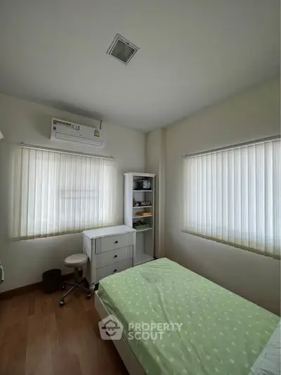 Cozy bedroom with natural light, featuring a single bed, air conditioning, and wooden flooring.