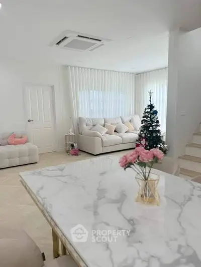 Elegant living room with marble table, cozy sofas, and a small decorated Christmas tree.