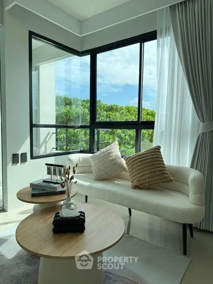 Bright living room with modern decor and large windows offering lush green views.