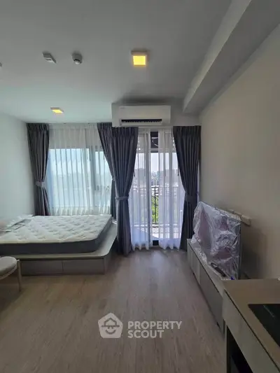 Modern bedroom with large windows and balcony access, featuring sleek furnishings and natural light.