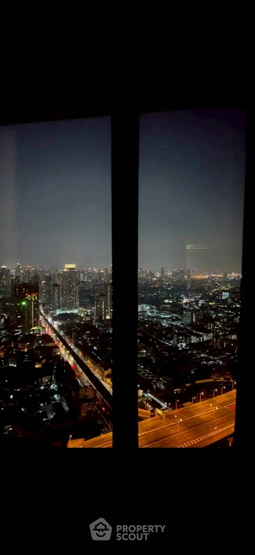 Stunning cityscape view from high-rise window at night, showcasing vibrant urban lights.