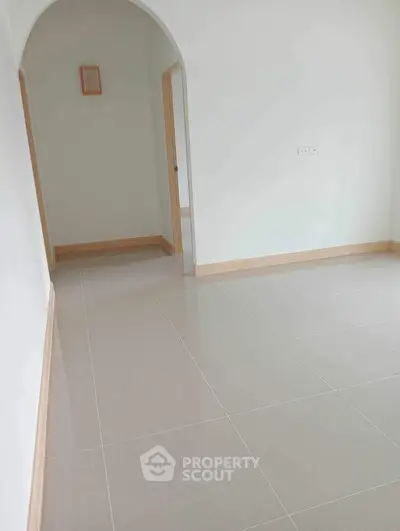 Spacious empty room with arched doorway and tiled flooring, perfect for customization.