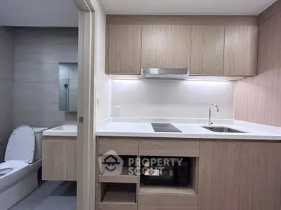 Modern kitchen with sleek cabinetry and adjacent bathroom in a compact apartment layout.