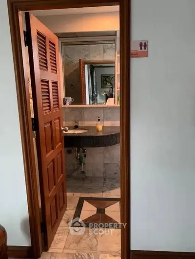 Charming bathroom with elegant marble flooring and wooden door, featuring a stylish vanity area.