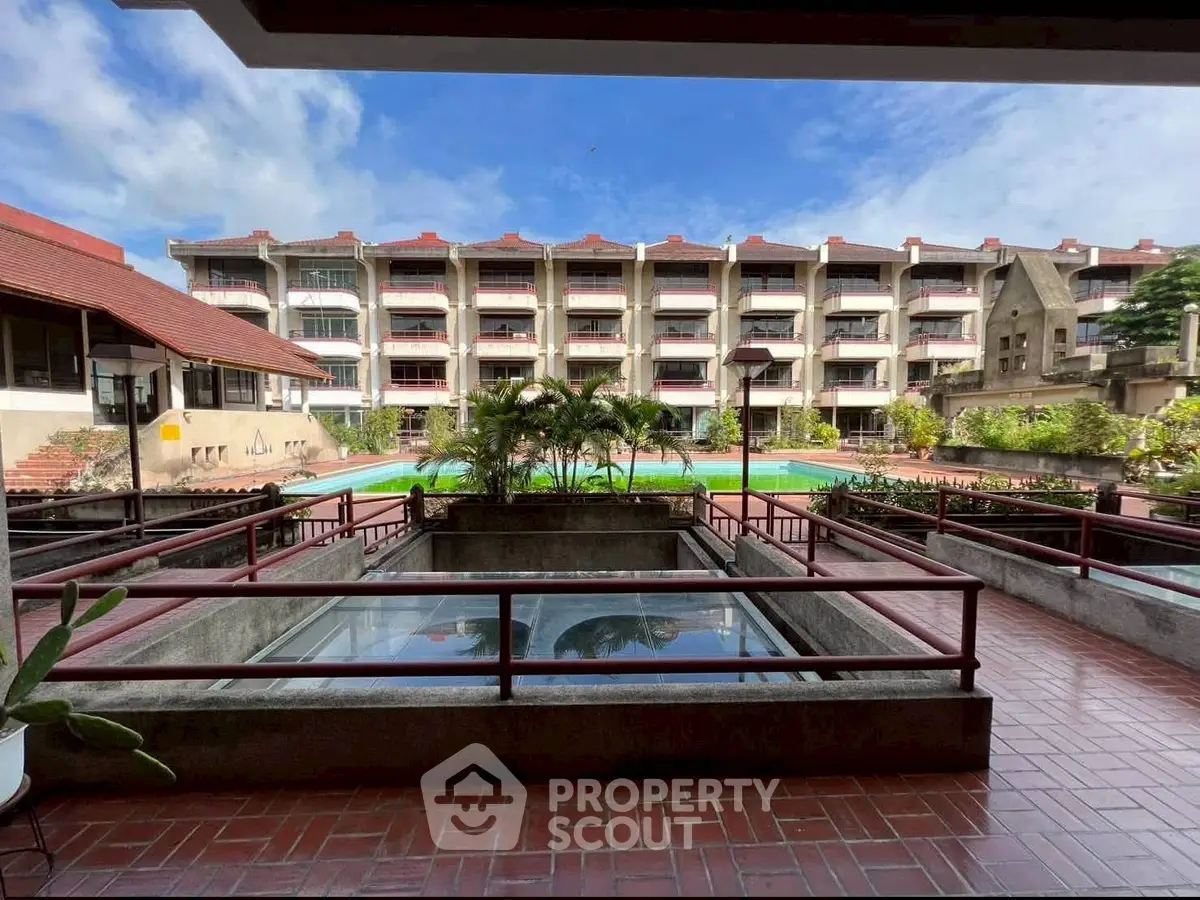 Spacious residential complex with pool and lush greenery under a clear blue sky.