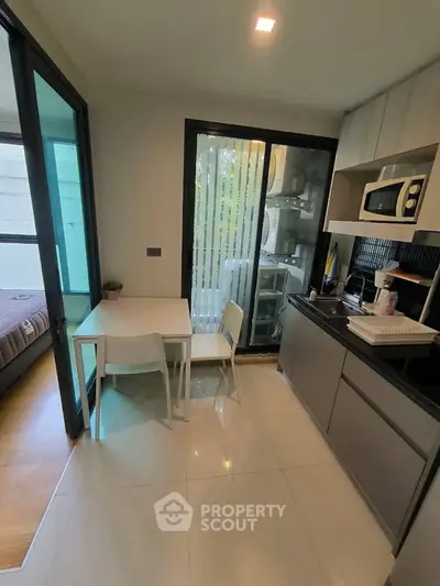Modern compact kitchen with dining area and view into bedroom, featuring sleek cabinetry and appliances.