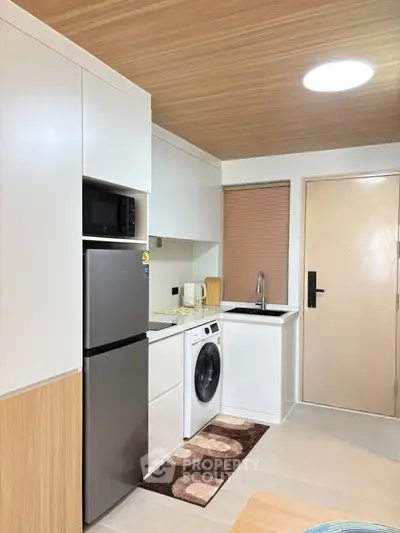 Modern kitchen with sleek appliances and wood accents, featuring a washing machine and fridge.