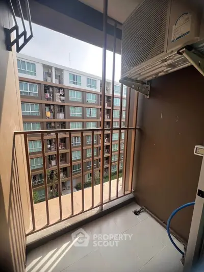 Compact balcony with air conditioning unit overlooking modern apartment complex.