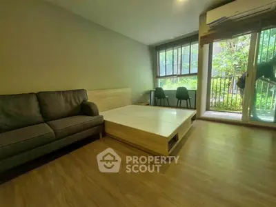Modern living room with sofa, wooden flooring, and large window overlooking greenery.