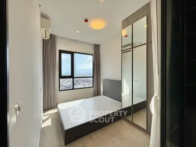 Modern bedroom with large window and city view, featuring mirrored wardrobe and minimalist design.