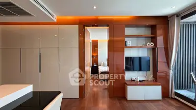 Modern living room with sleek wooden accents and built-in TV unit, leading to a cozy bedroom.