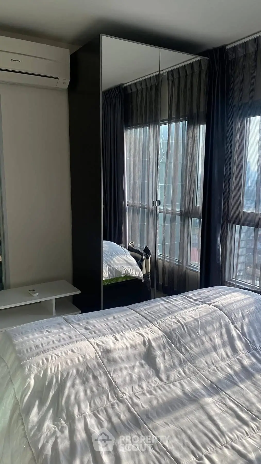 Modern bedroom with large windows and mirrored wardrobe reflecting natural light.