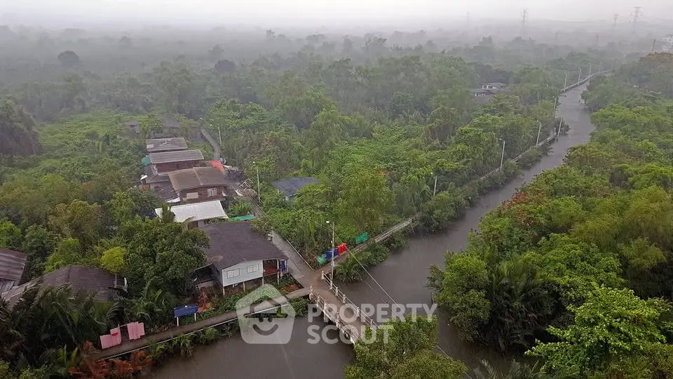 Scenic aerial view of lush green residential area with winding river and misty atmosphere.