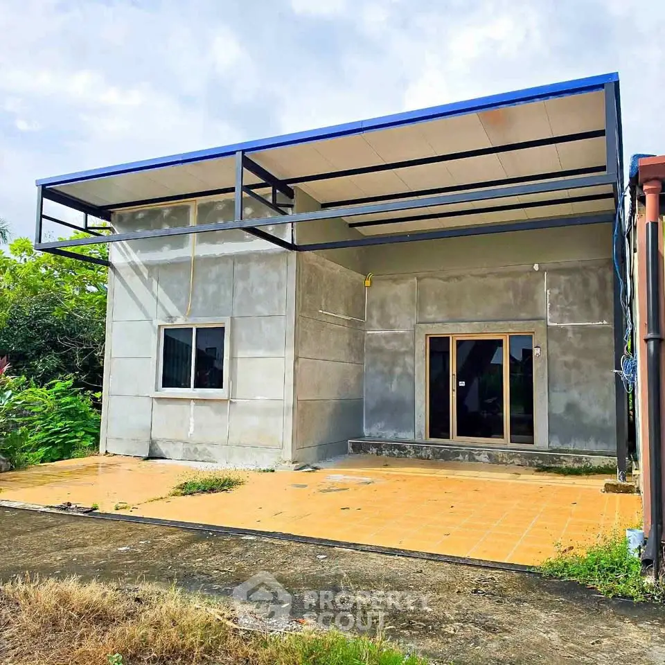 Modern minimalist single-story house with unfinished exterior and spacious front patio.