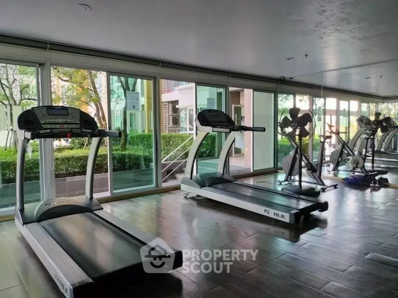 Modern gym with treadmills and large windows offering garden views.