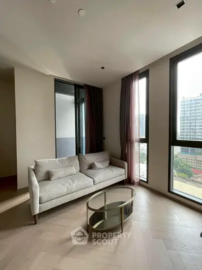 Modern living room with elegant sofa and glass coffee table, featuring large windows with city view.