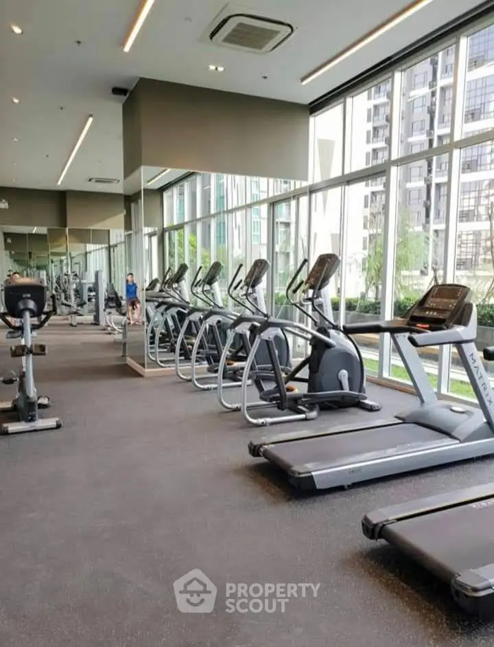 Modern gym with state-of-the-art equipment and floor-to-ceiling windows in luxury building.