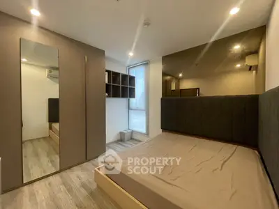 Modern bedroom with sleek design and ample natural light, featuring a large mirror and stylish storage solutions.