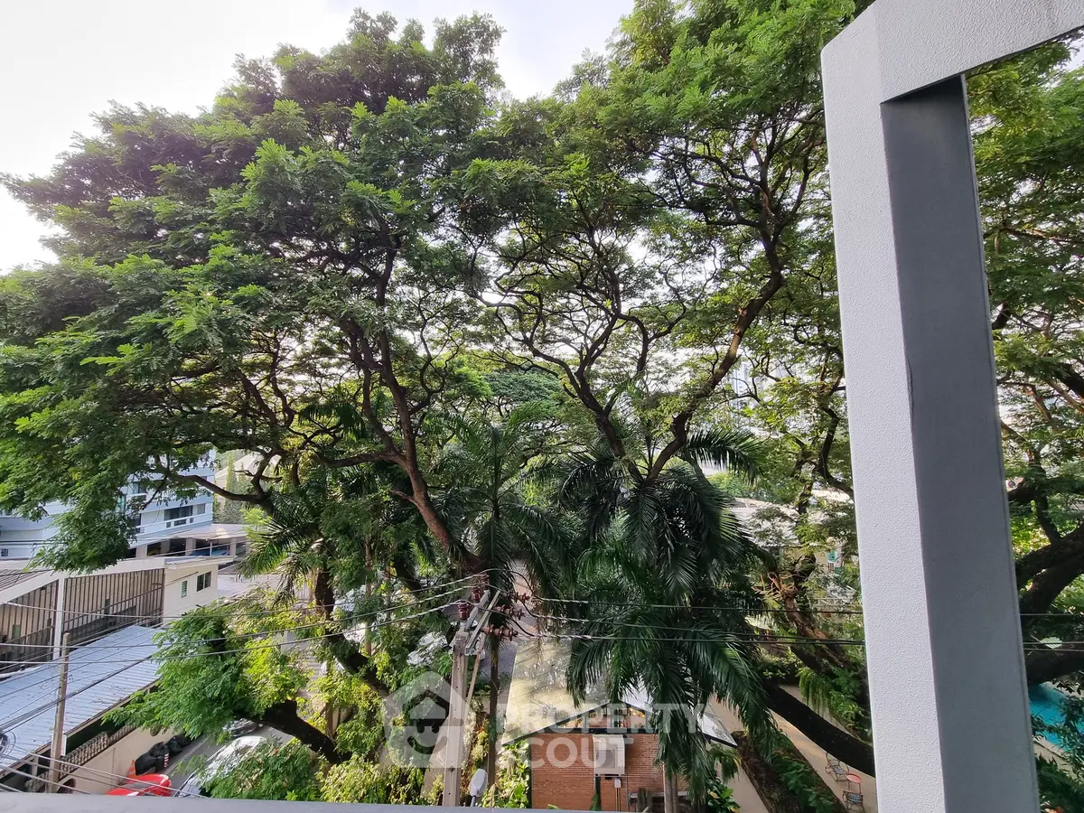 Lush green view from a modern balcony overlooking trees and urban landscape.