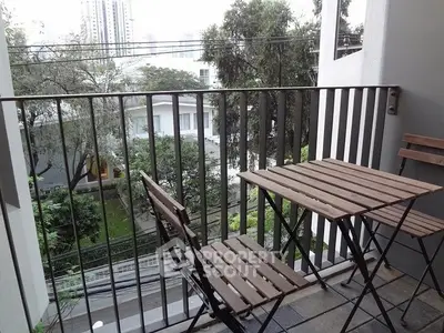 Charming balcony with wooden furniture and lush green view in urban setting.