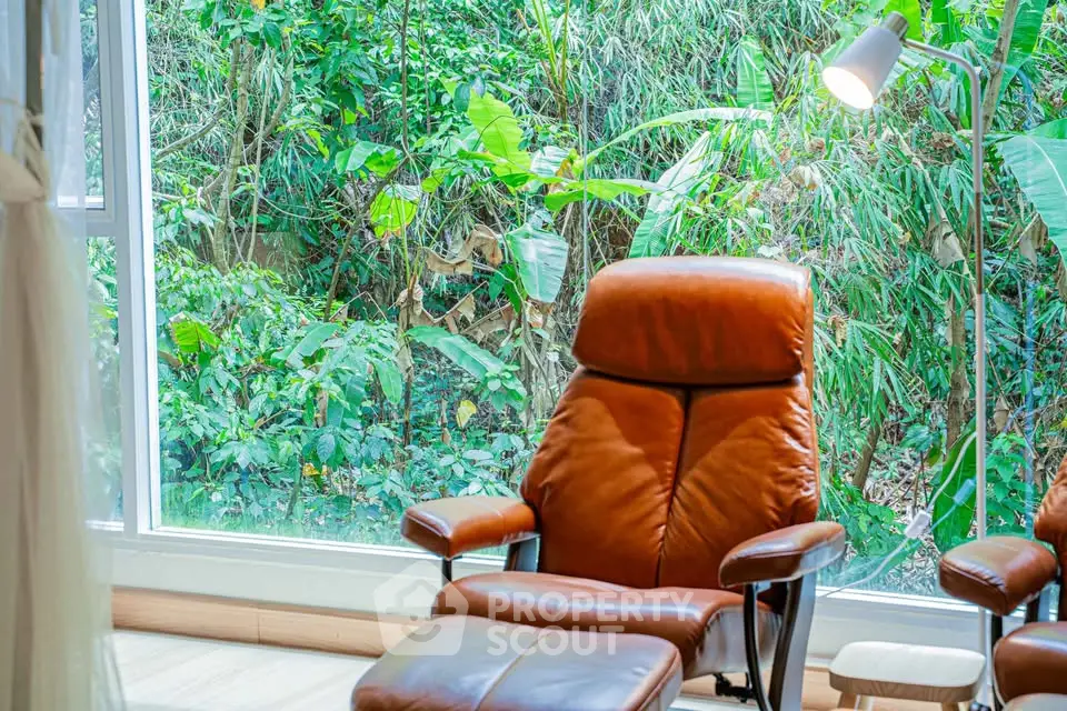 Cozy living room with leather chair and lush garden view through large window.