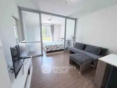 Modern living room with sliding glass doors leading to a bright bedroom, featuring sleek furniture and natural light.