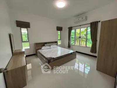 Spacious bedroom with modern furnishings and large windows offering lush green views.